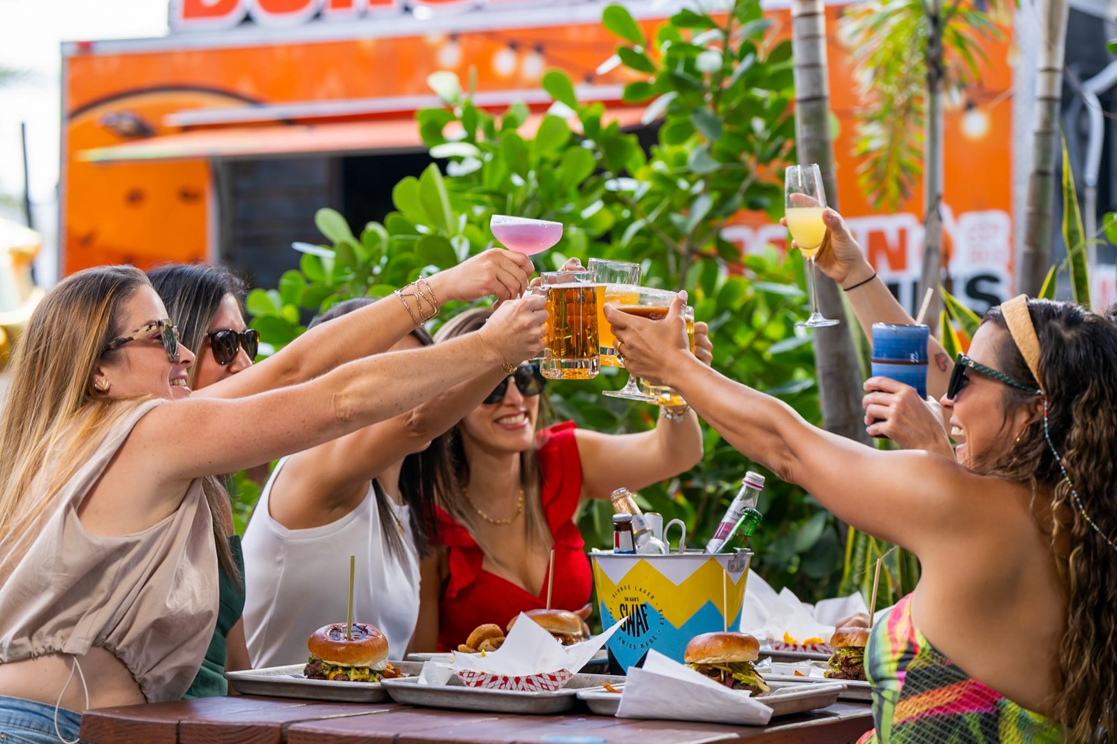 Friends toasting drinks over Latin Fixin's burgers at The Doral Yard